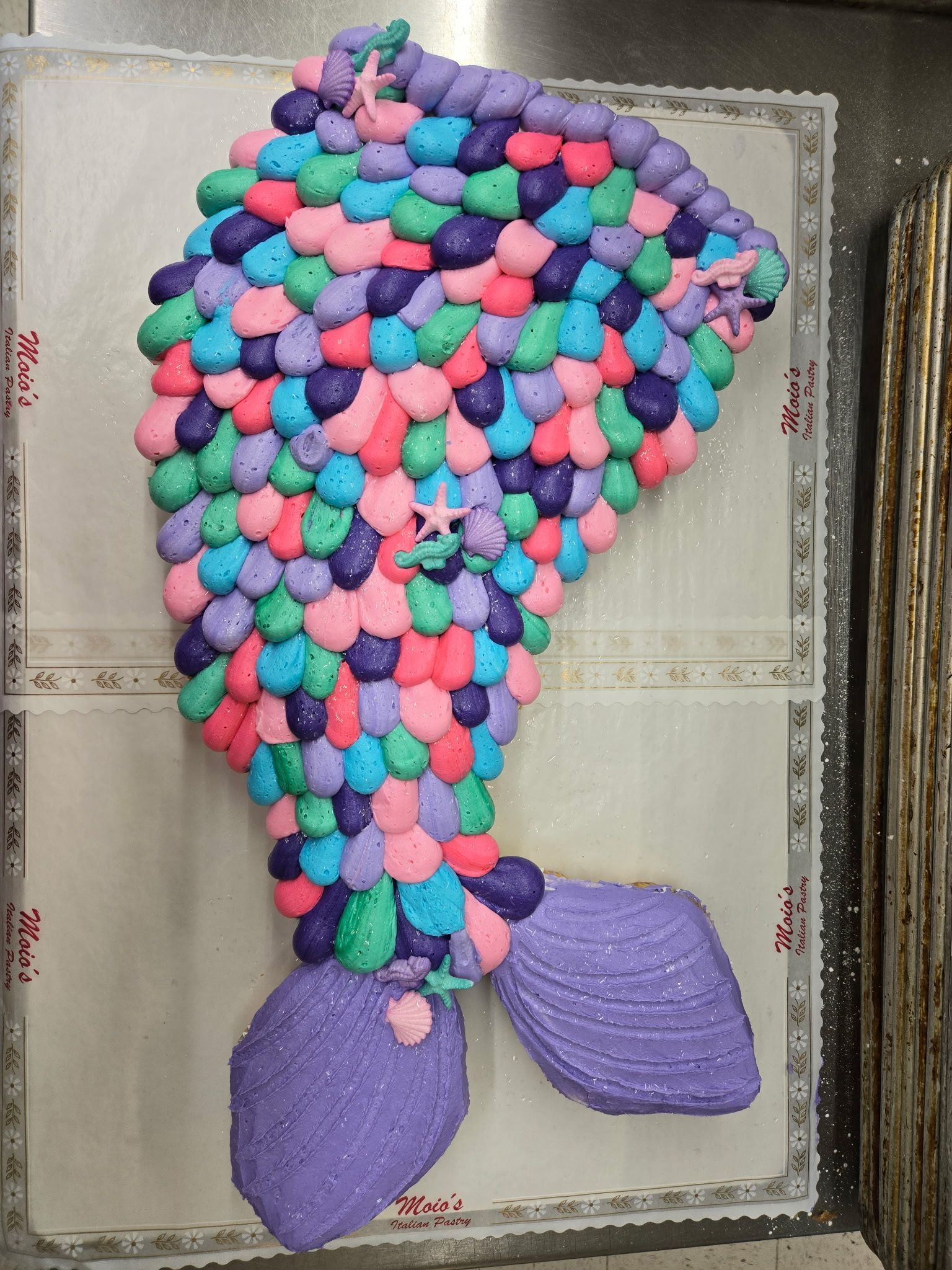 Mermaid tail cake decorated with colorful candies and frosting.