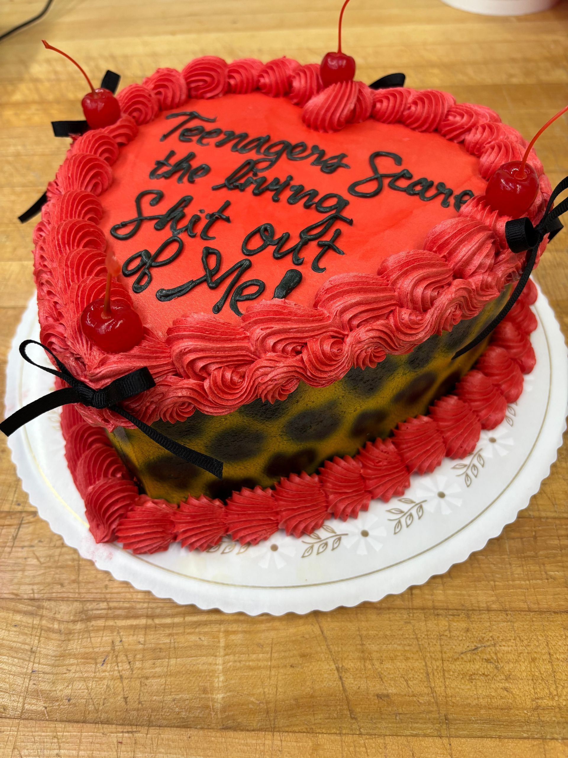Heart-shaped cake with red frosting, black lettering, and cherries; leopard print sides.