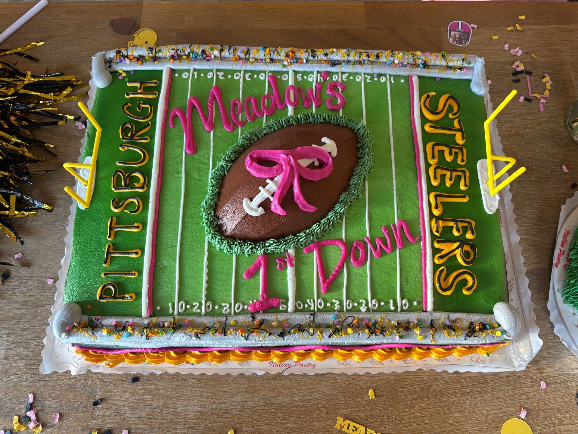 Football field cake decorated in pink, green, and gold.