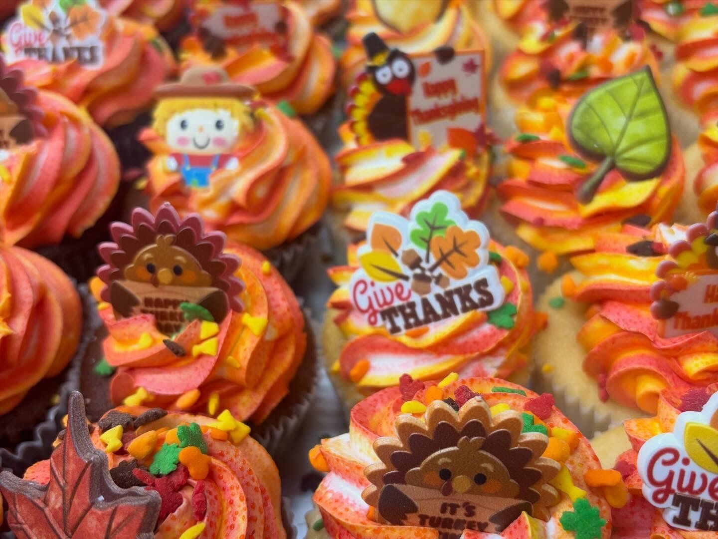 Thanksgiving cupcakes with orange and yellow frosting, decorated with fall-themed toppers.