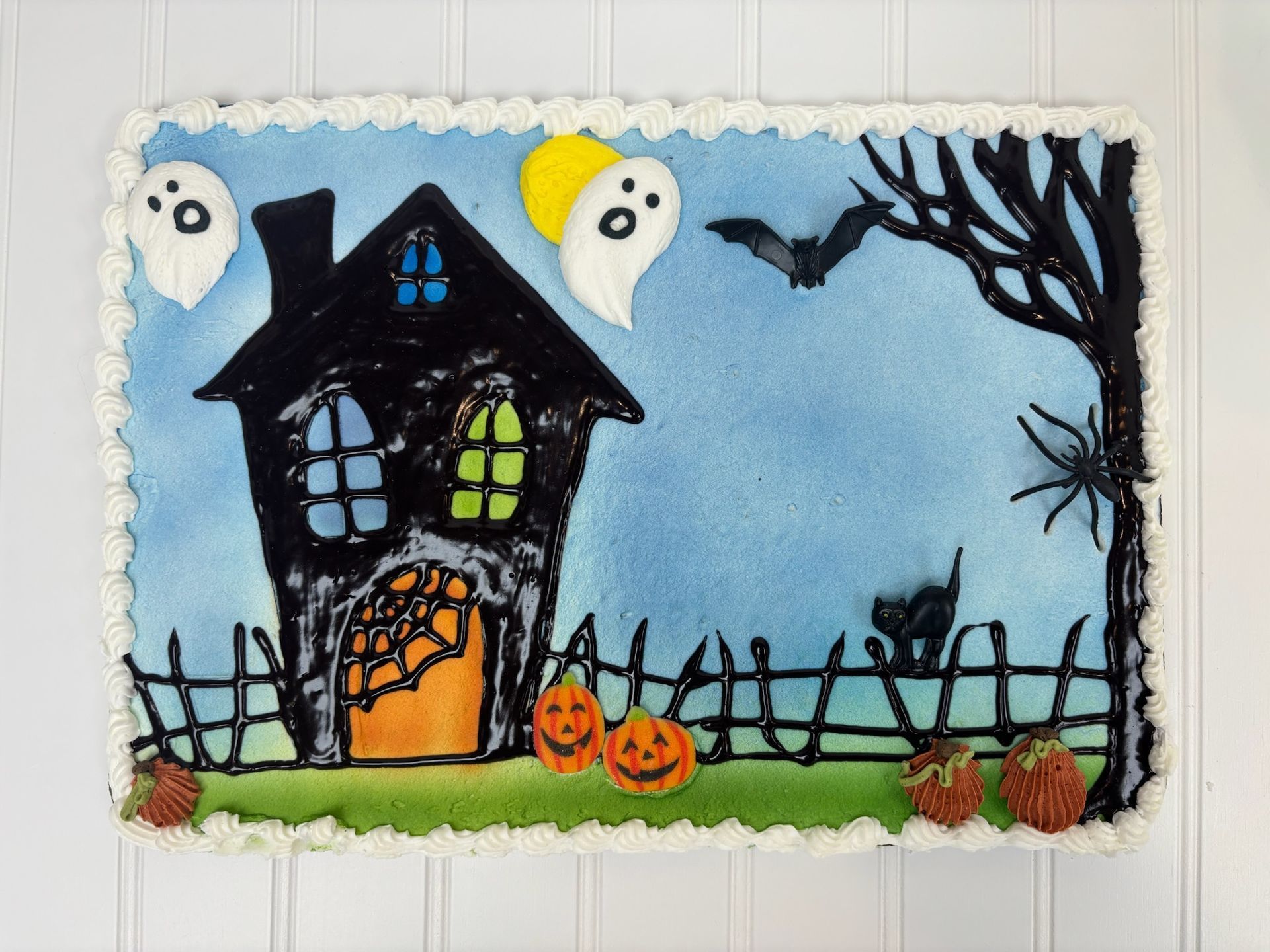 Halloween cake with a haunted house, ghosts, pumpkins, and a black cat.