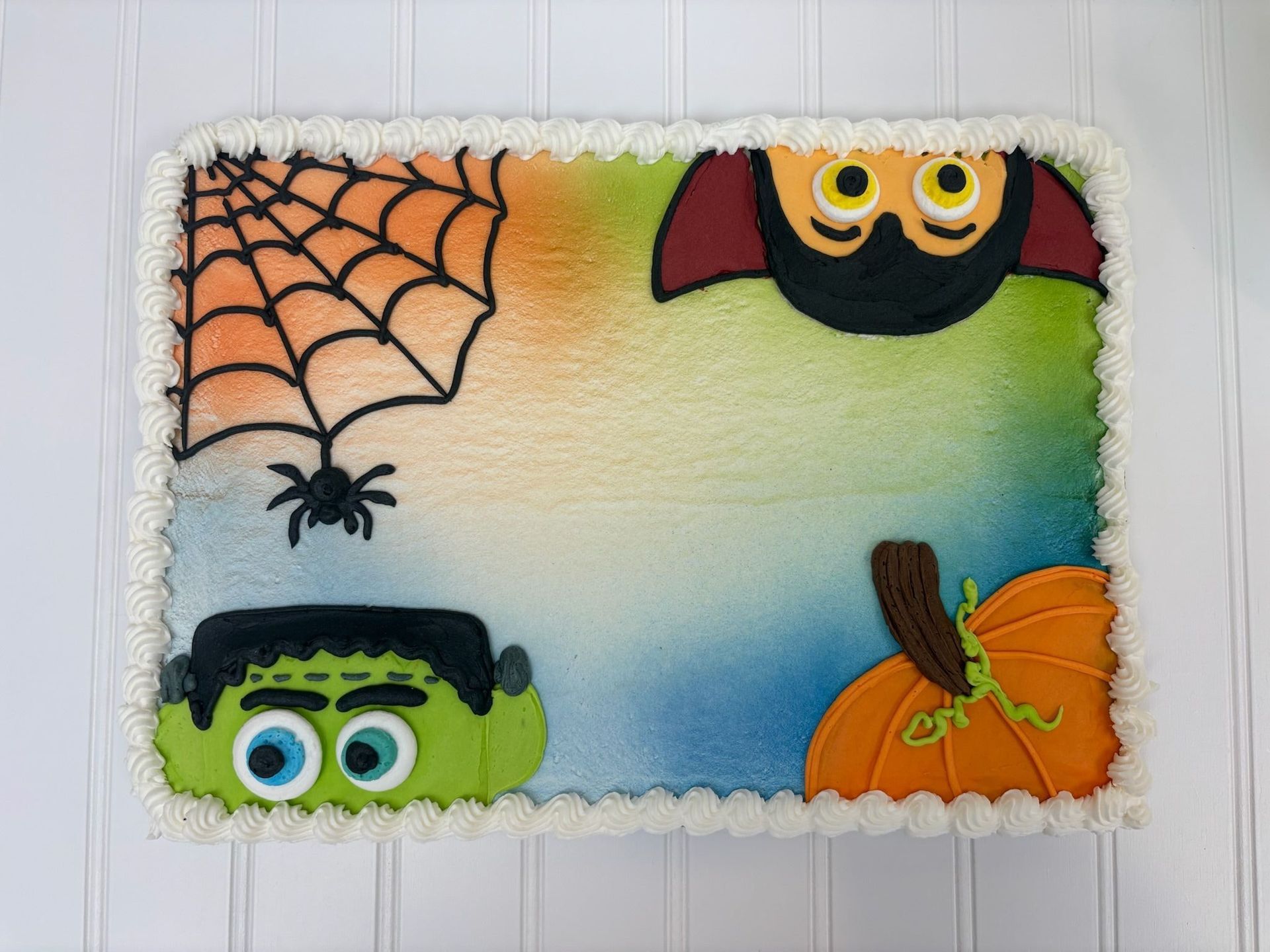 Halloween cake with spiderweb, bat, Frankenstein, and pumpkin decorations.