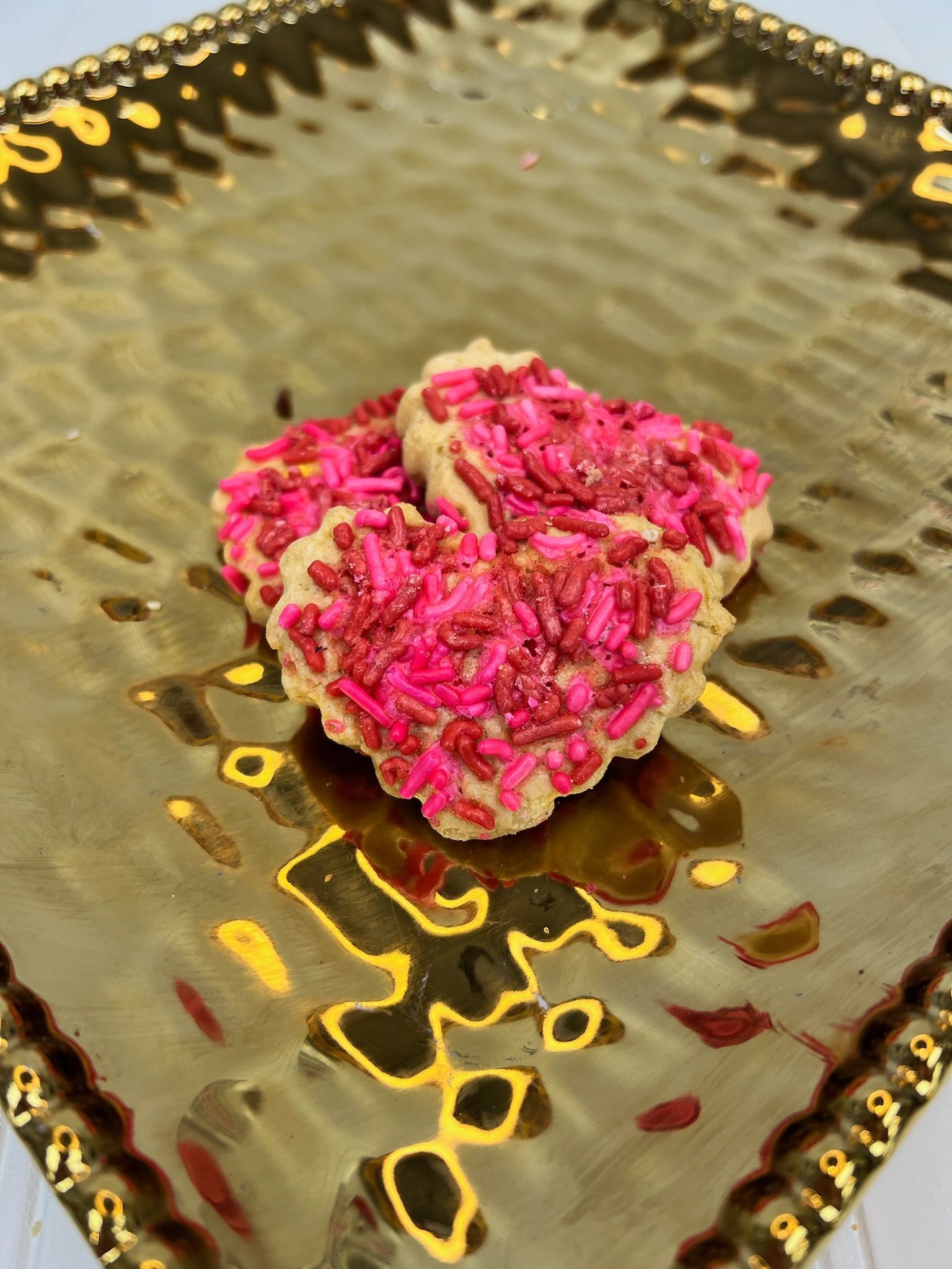Heart-shaped cookies covered in pink sprinkles on a gold, textured plate.