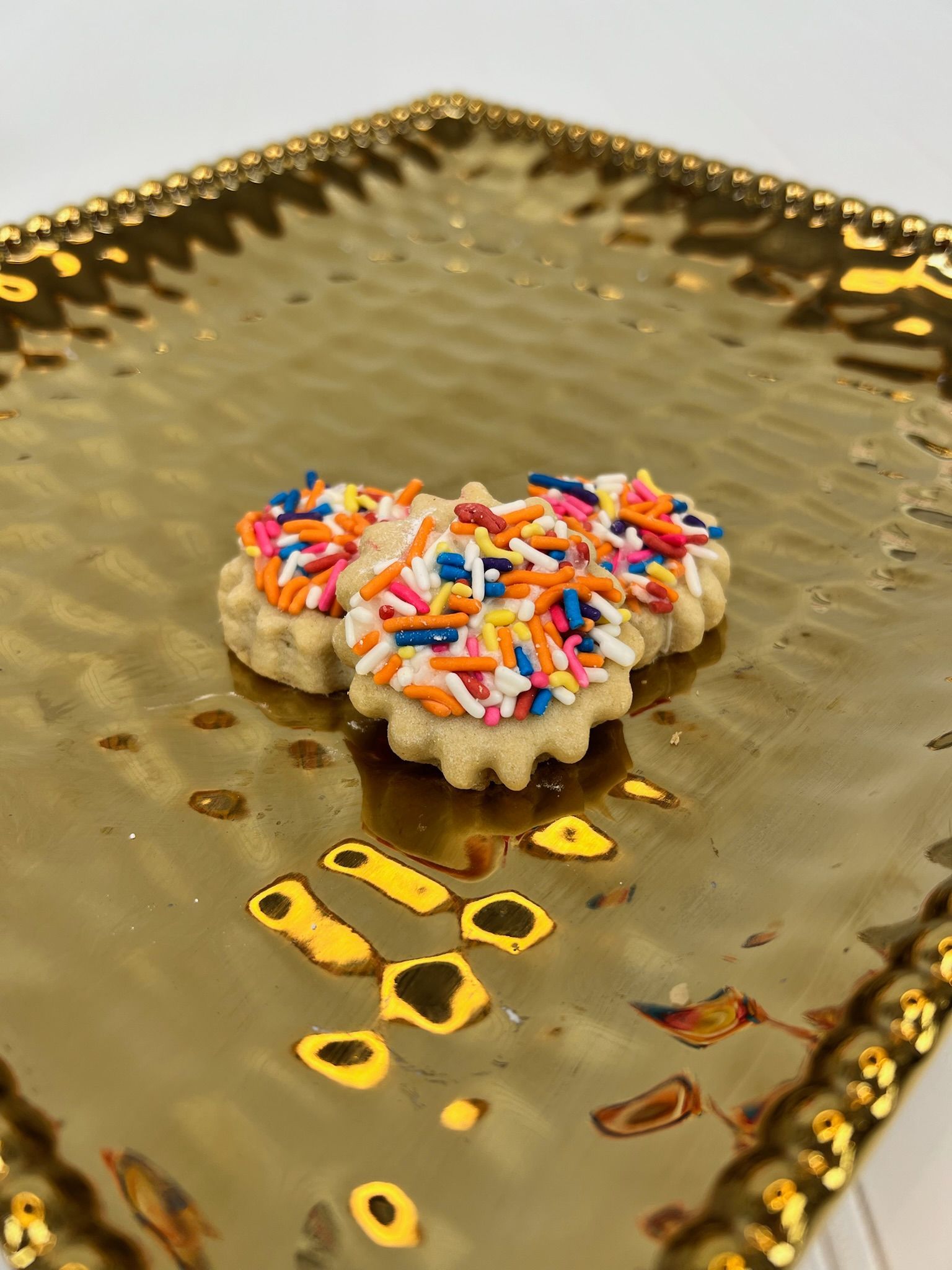Three flower-shaped cookies with sprinkles on a gold platter.