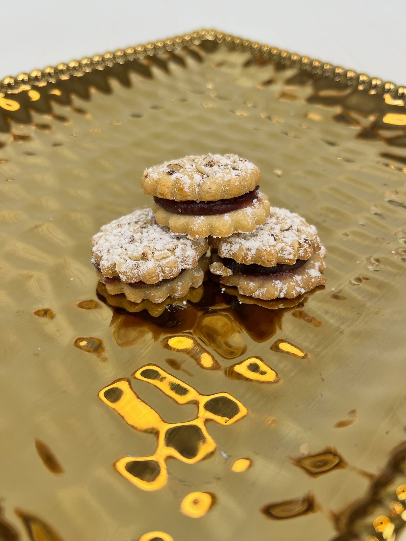 Three sandwich cookies with jam filling, dusted with powdered sugar, on a gold tray.