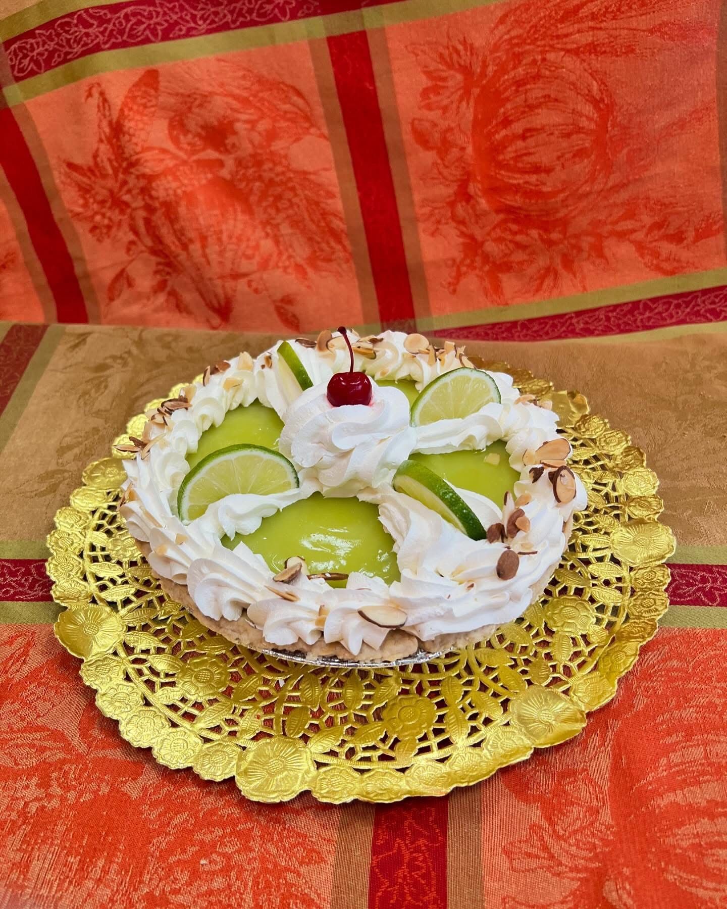 Key lime pie on a gold doily, topped with whipped cream, lime slices, and a cherry.