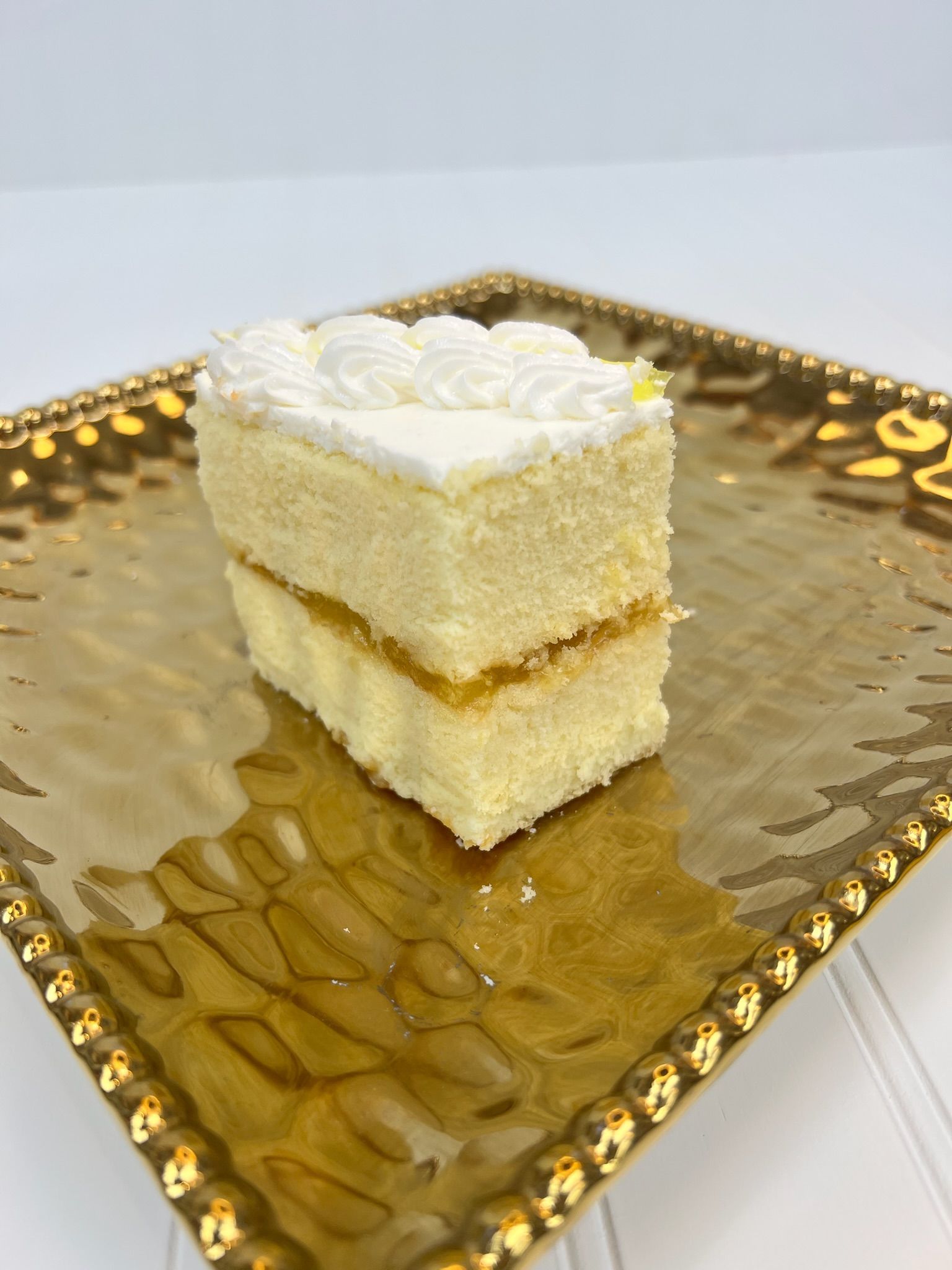 Slice of layered cake on a gold, textured square plate. White frosting on top, yellow filling in between layers.