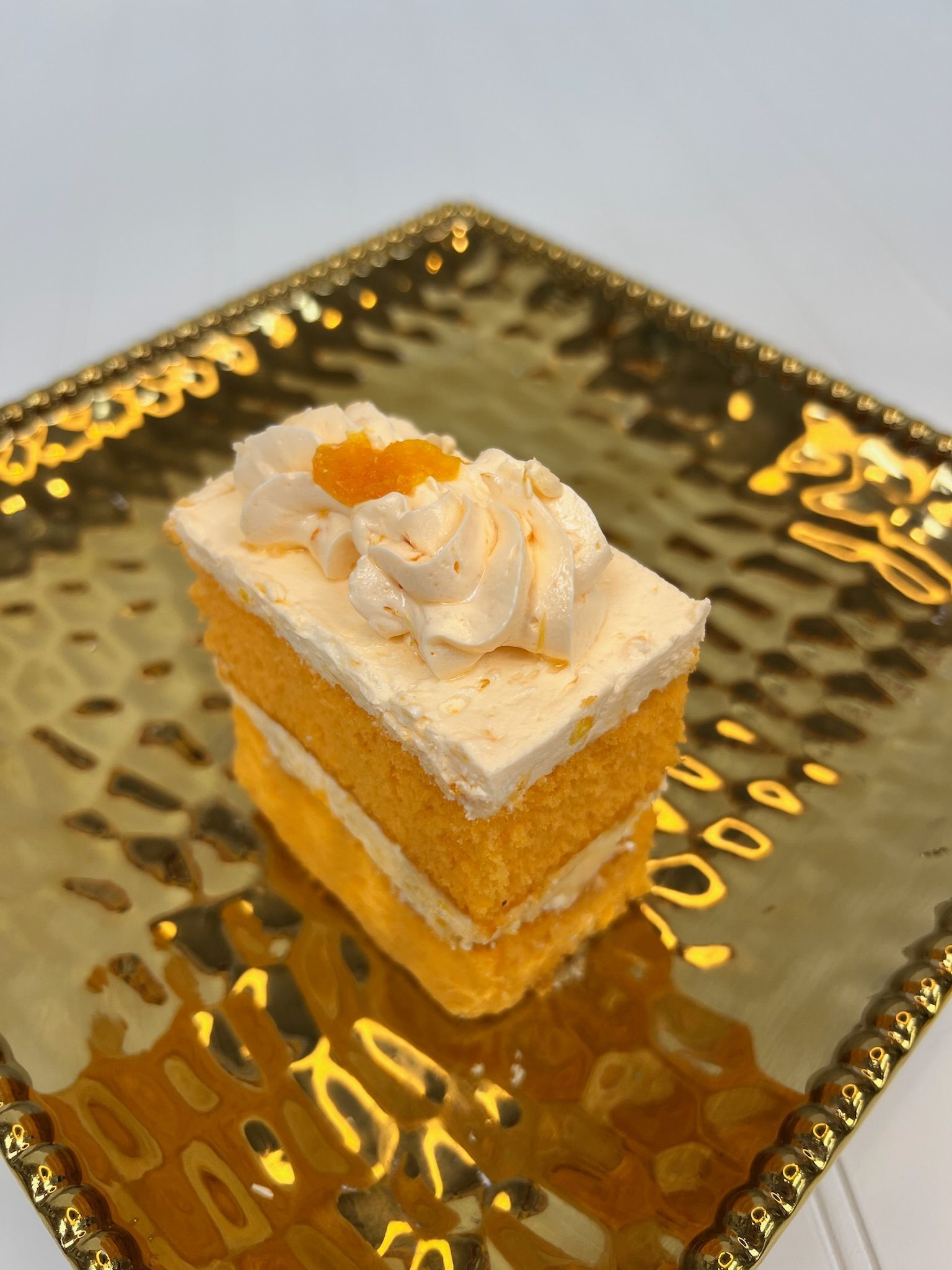 Slice of layered orange cake with frosting and a golden plate.