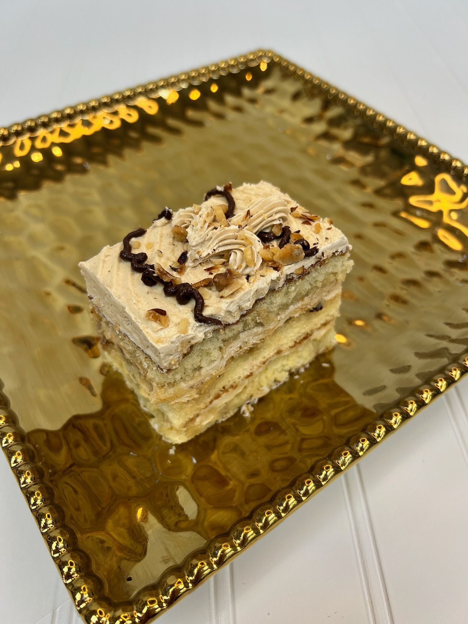 Slice of layered cake with frosting and chocolate drizzle on a gold platter.