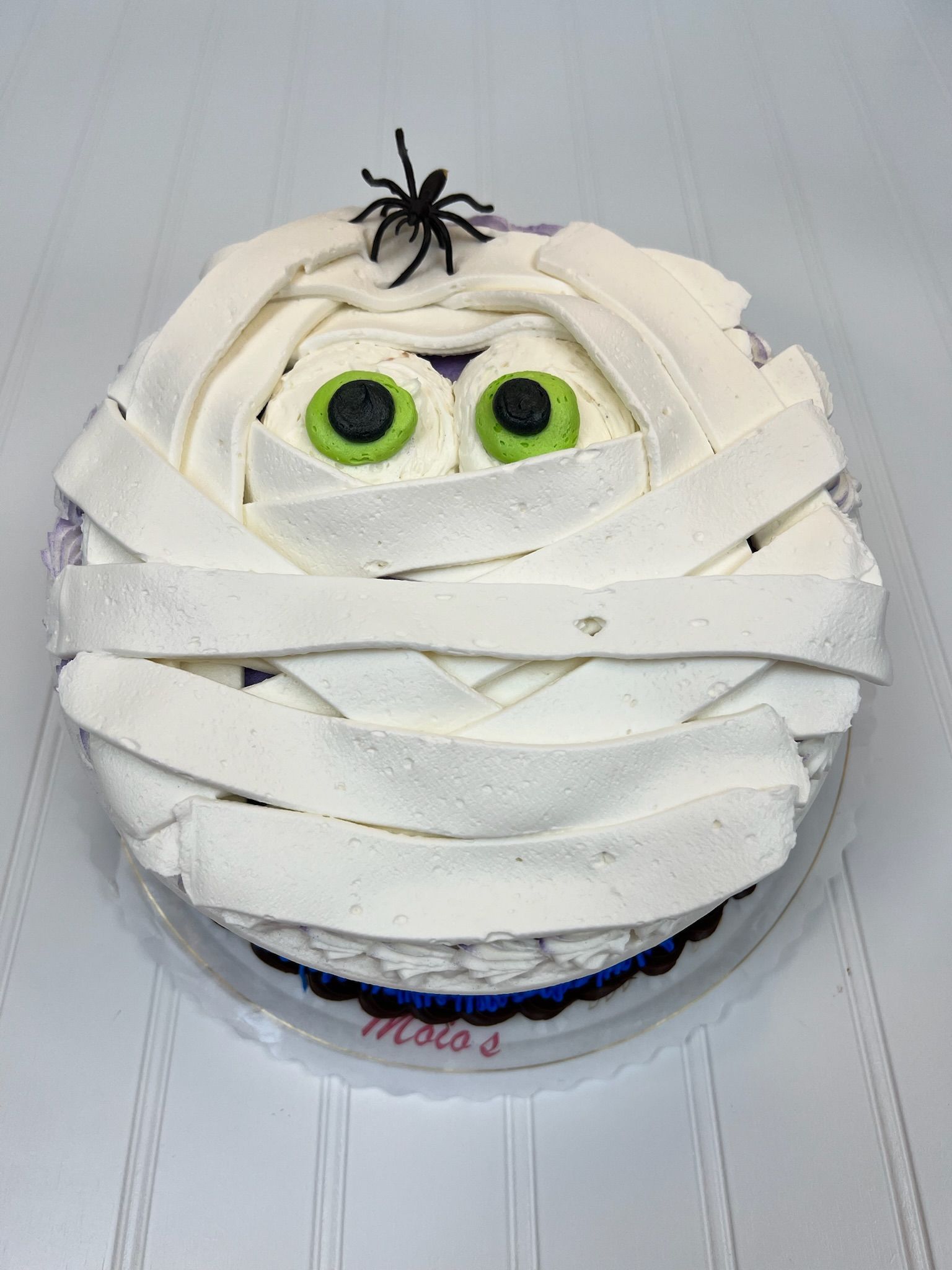 Mummy cake with white frosting bandages, green-eyed eyeballs, and a black spider on top.