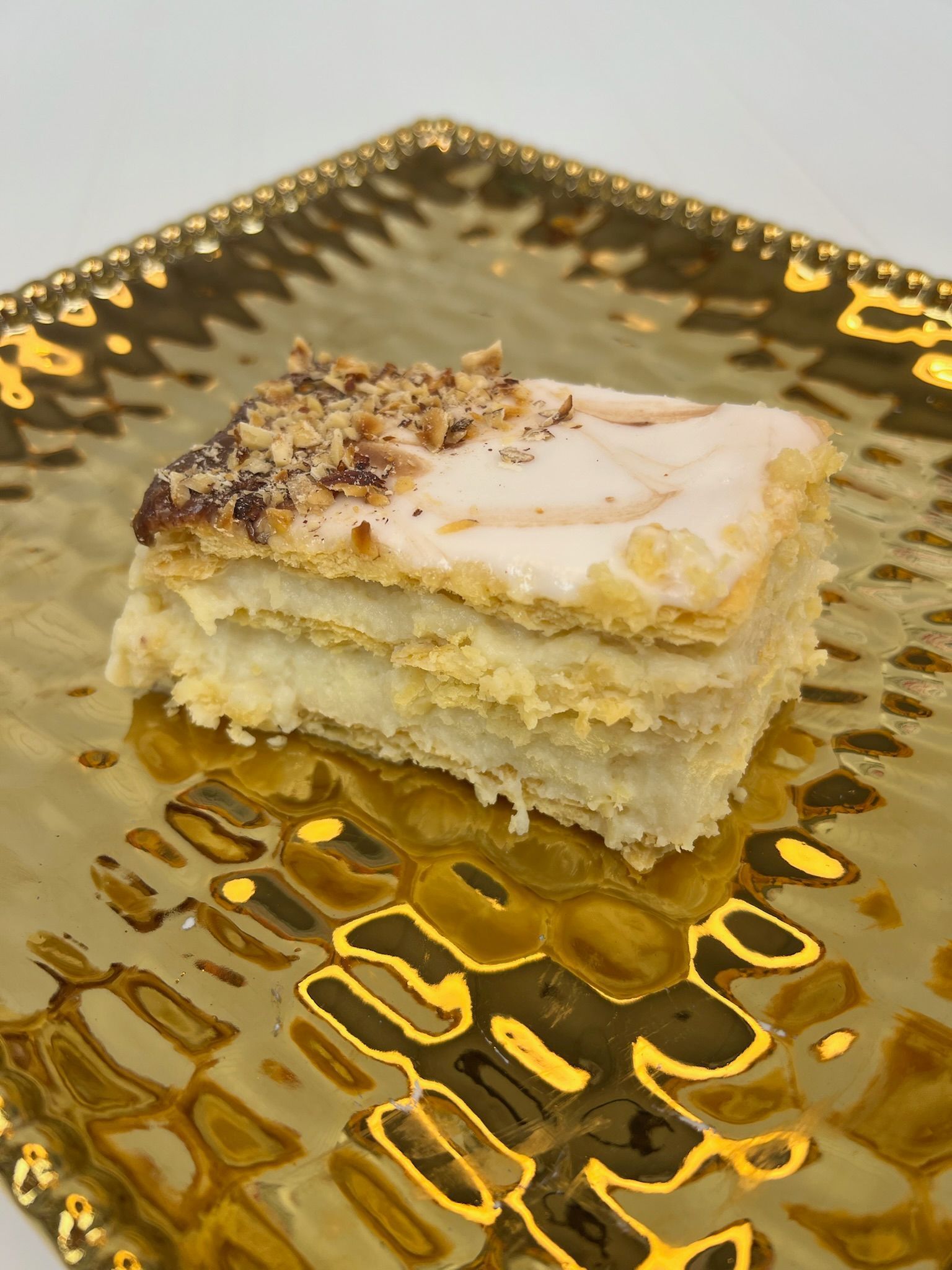 Cake slice on a golden plate, layers of pastry with frosting and nuts.