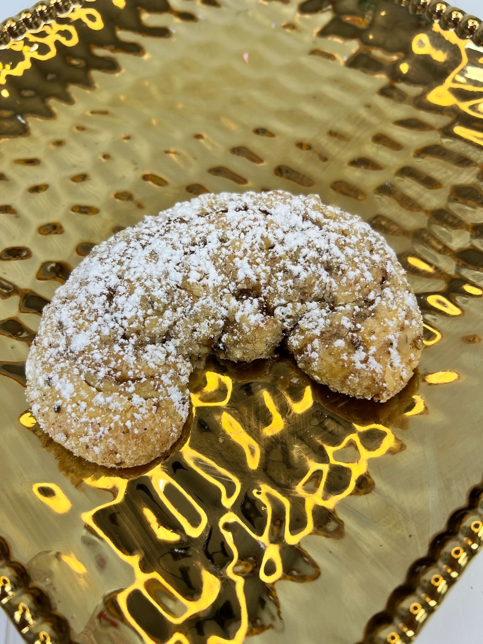 A crescent-shaped cookie dusted with powdered sugar rests on a gold, patterned plate.