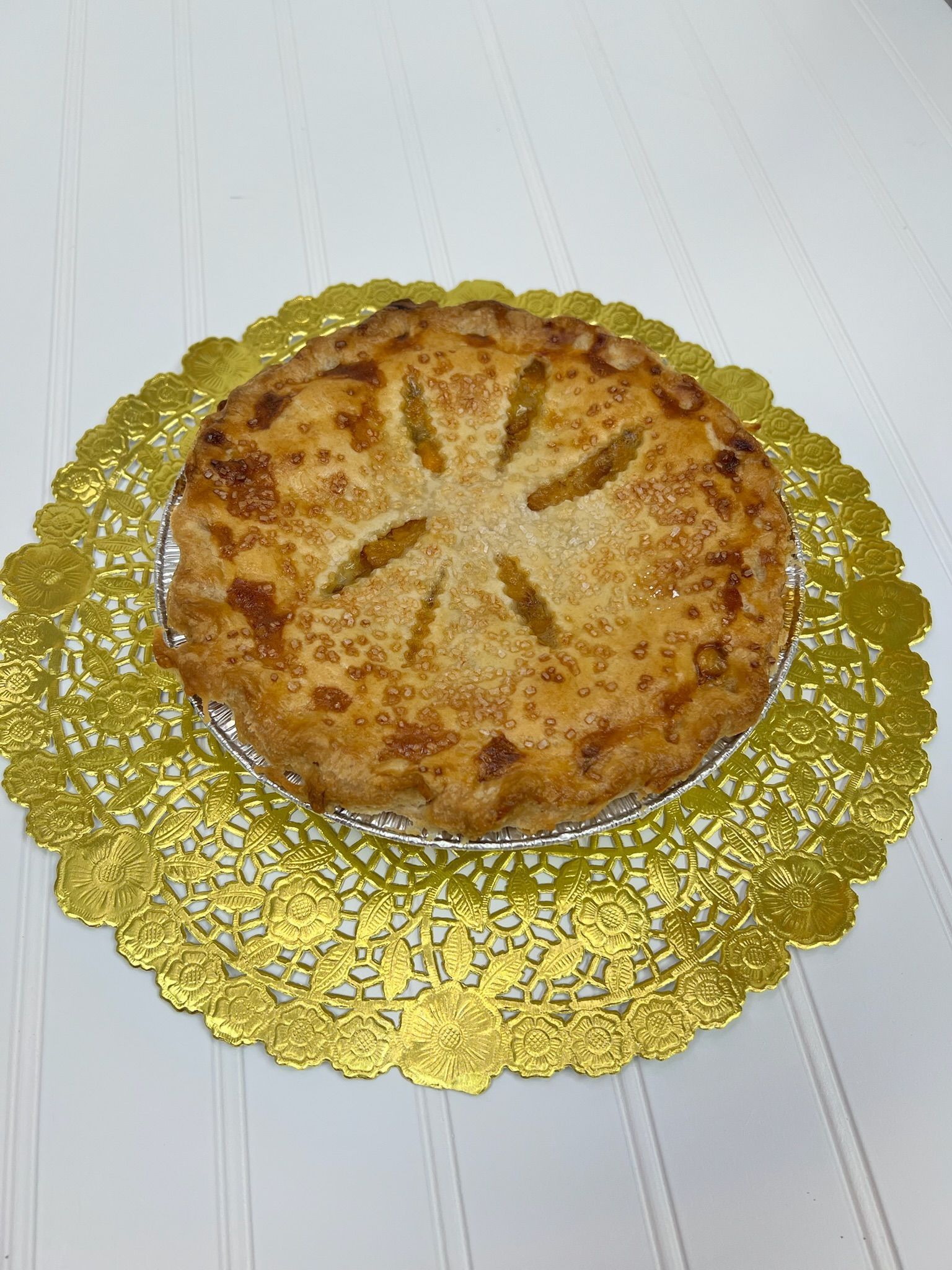 Apple pie on gold doily, baked golden crust with star cutouts on top, white wood background.