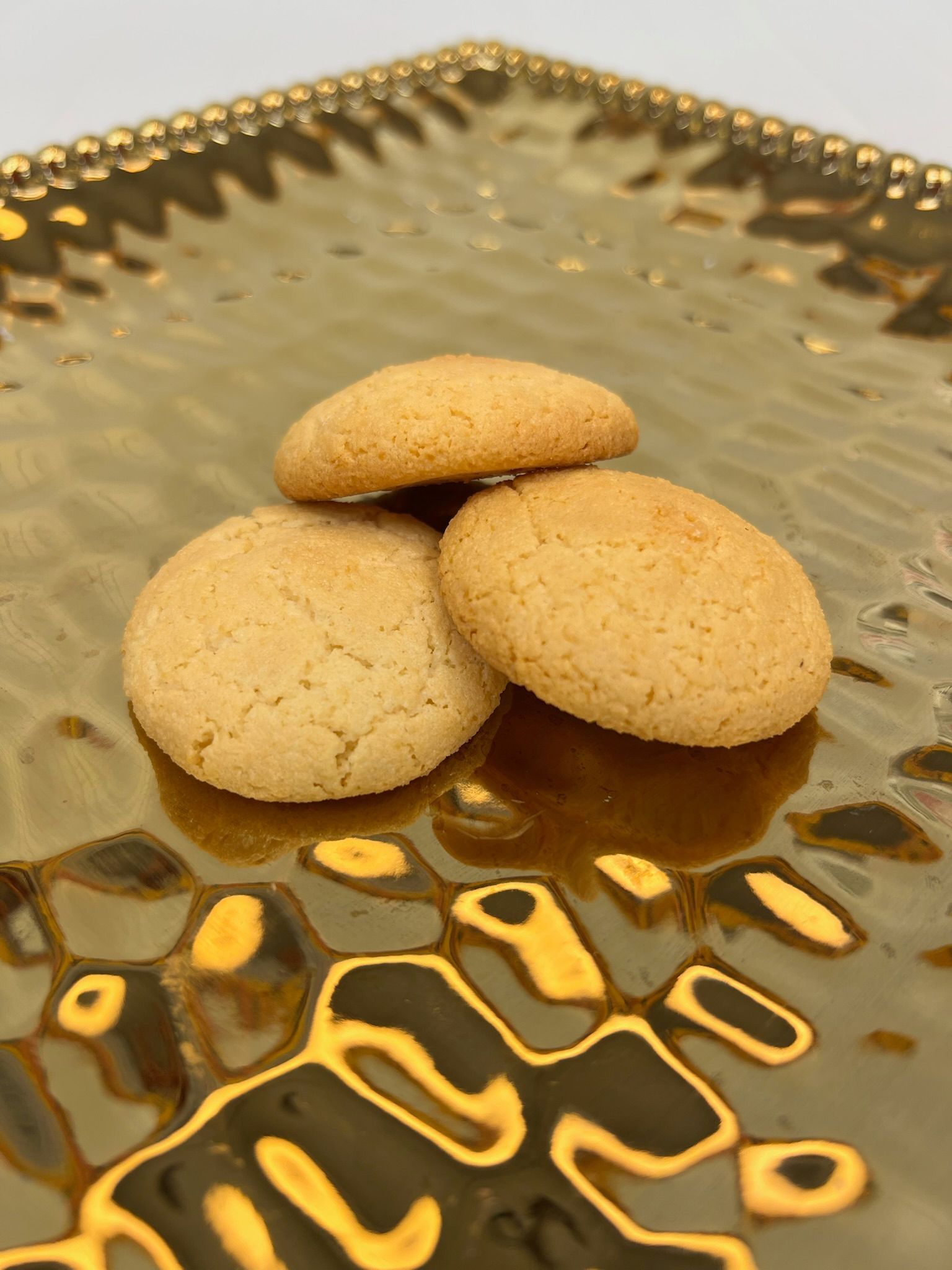 Three golden-brown cookies stacked on a textured gold plate.