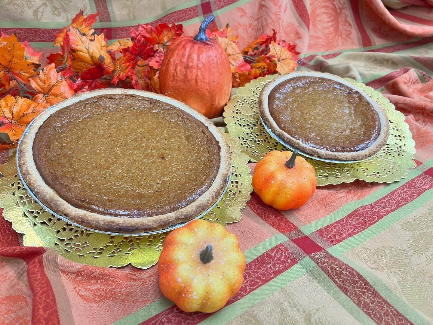 Two pumpkin pies and pumpkins on a fall-themed tablecloth.