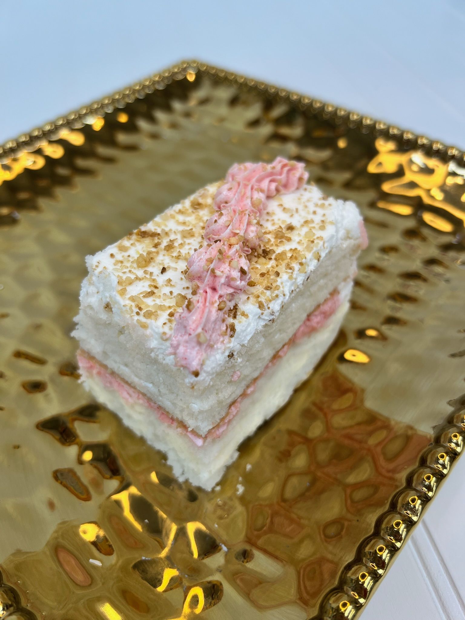 Slice of layered cake with pink frosting, topped with sprinkles, on a gold plate.