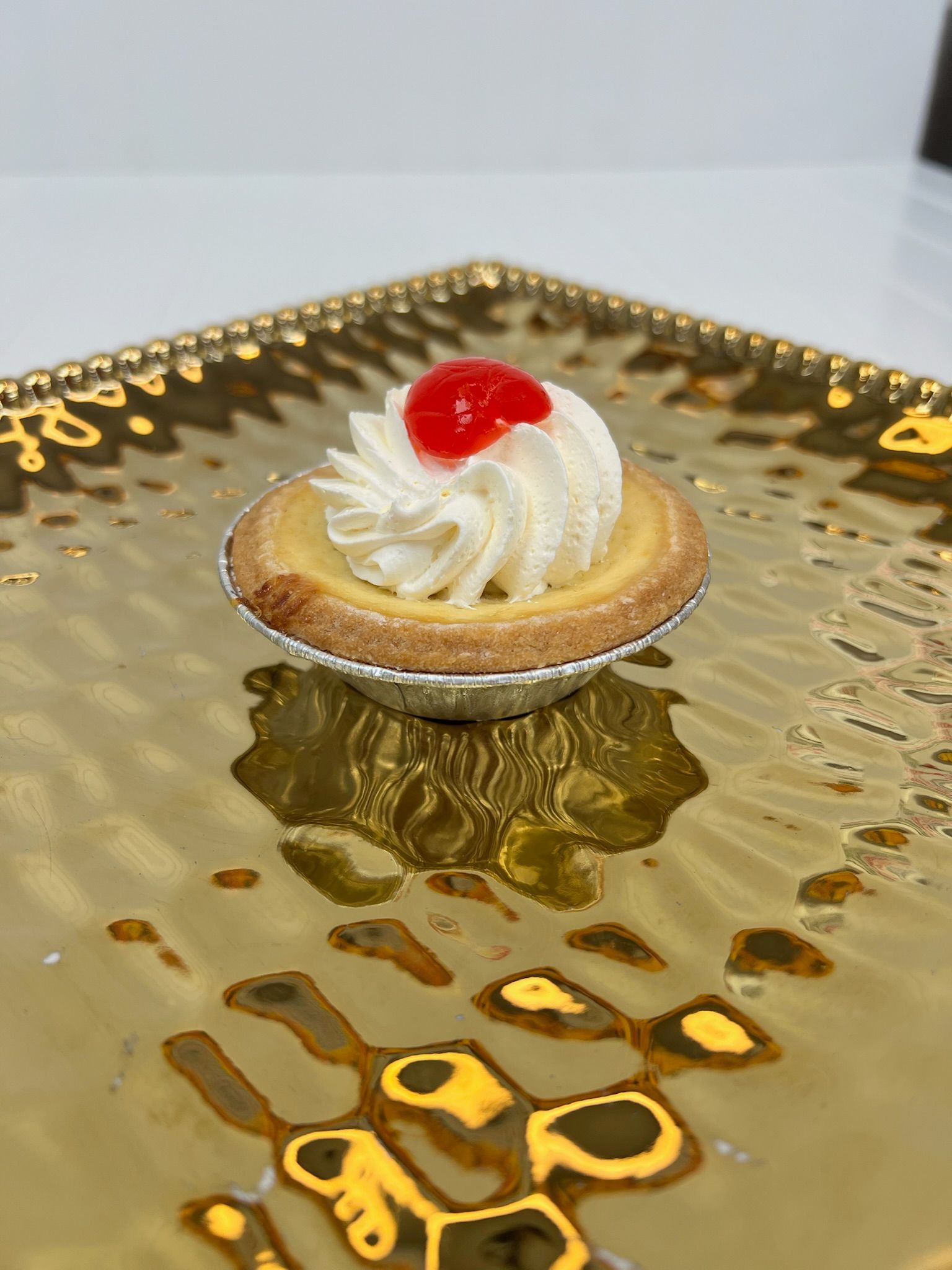 Mini tart with whipped cream and a cherry on a gold tray.