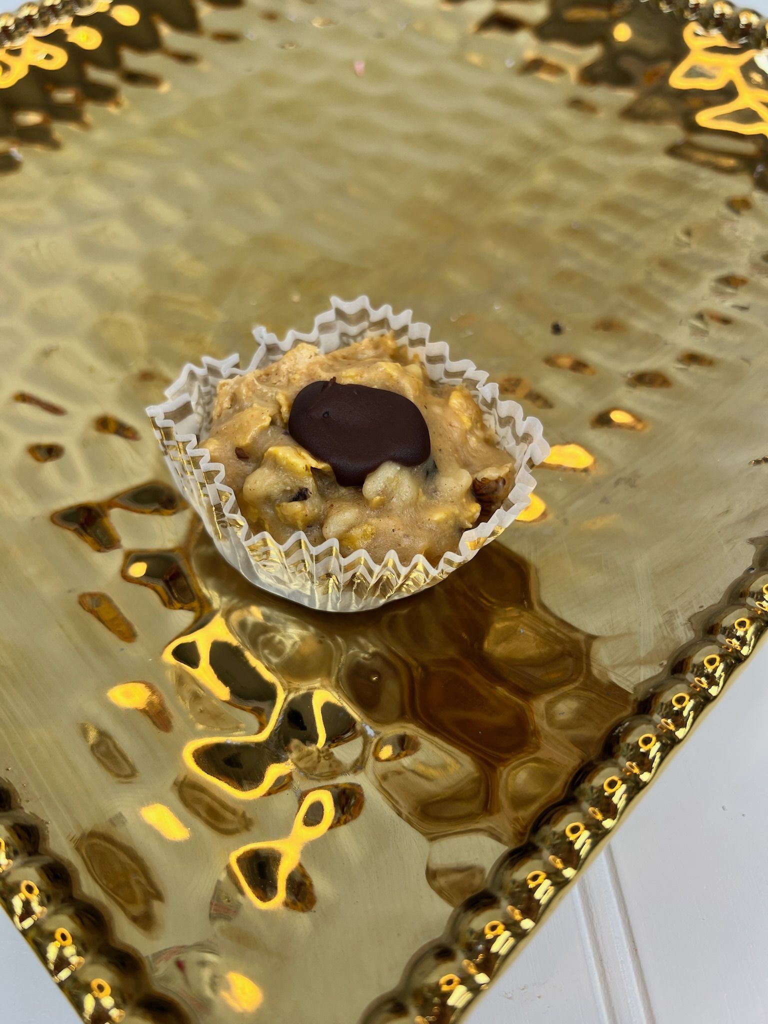 Cookie in a paper cup on a gold textured plate. Chocolate chip on top.