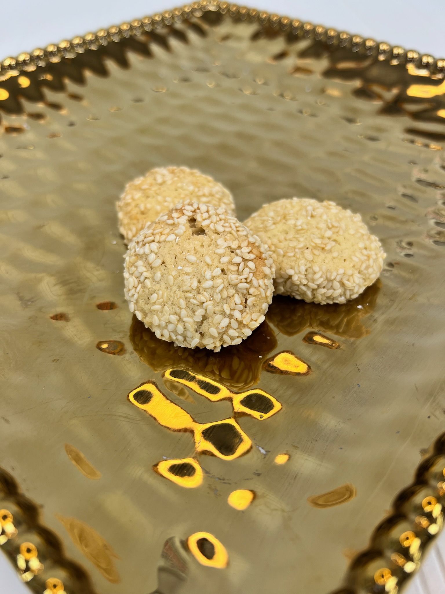 Three sesame-crusted cookies on a gold, textured, decorative platter.