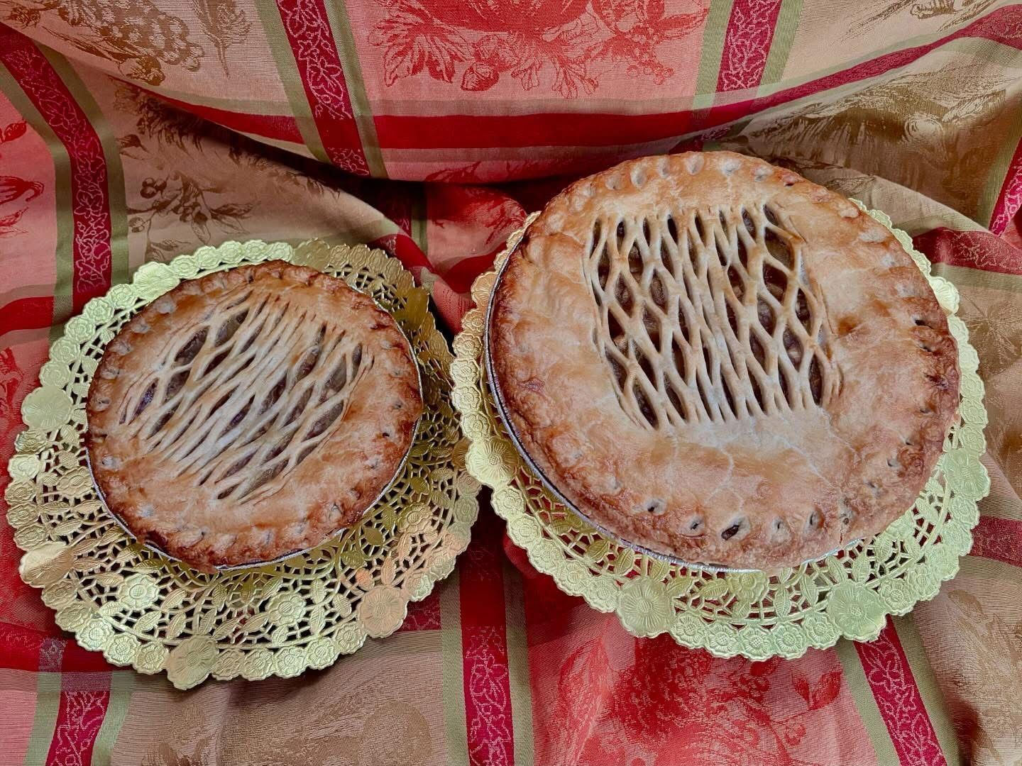 Two lattice-topped pies on gold paper doilies, set against a striped fabric with floral patterns.
