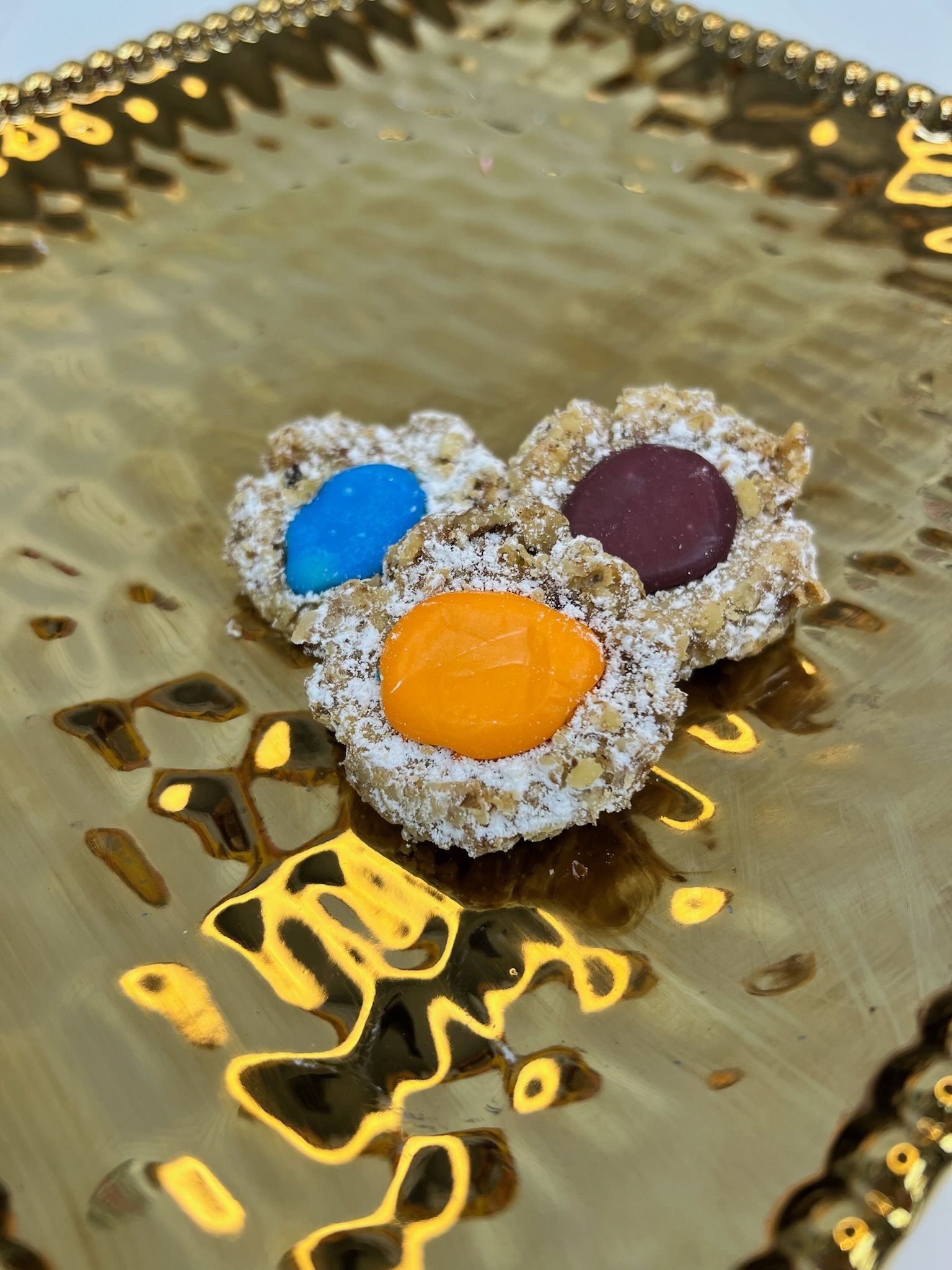 Three cookies with colorful candies, on a gold, textured tray.