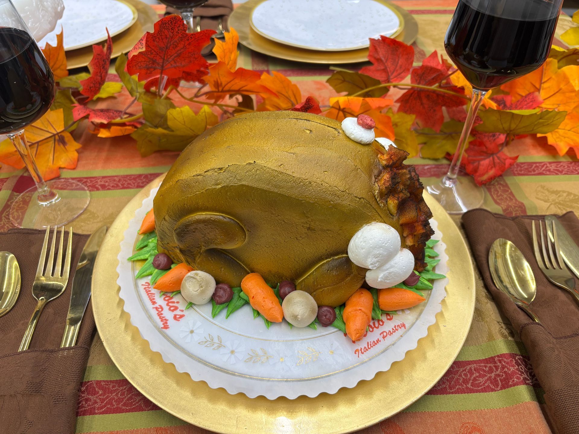 Thanksgiving cake shaped like a roasted turkey, carrots, and mushrooms on a decorated table with wine glasses and fall leaves.