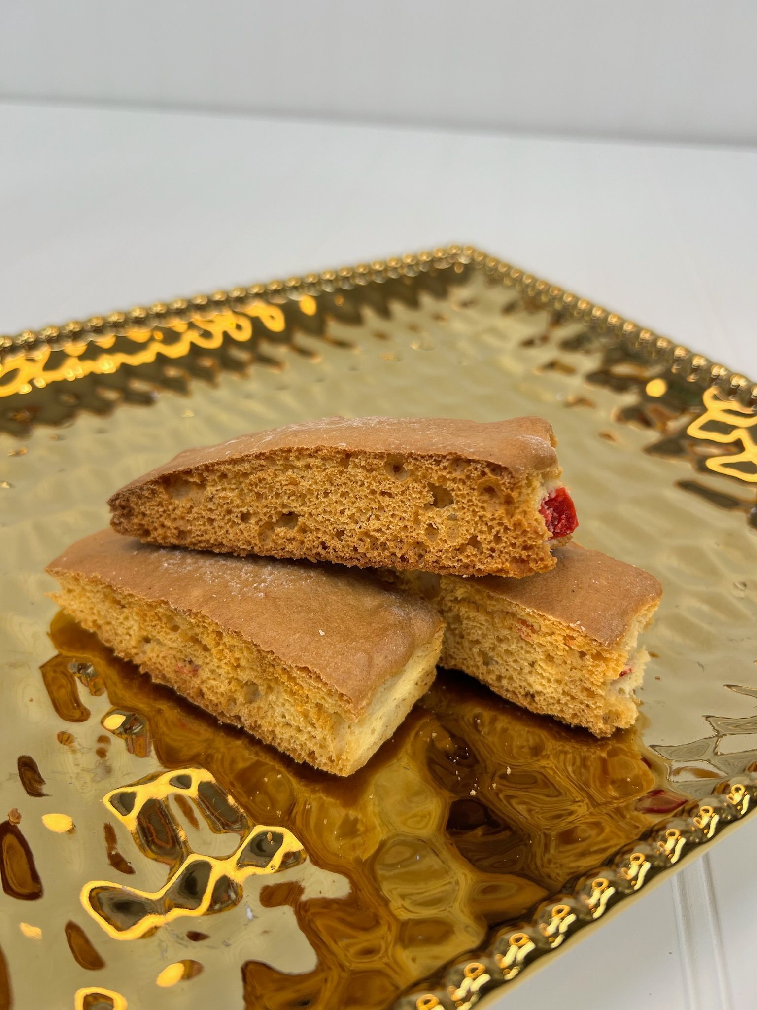 Three golden-brown biscotti on a gold, textured plate; one with a red fruit piece peeking out.
