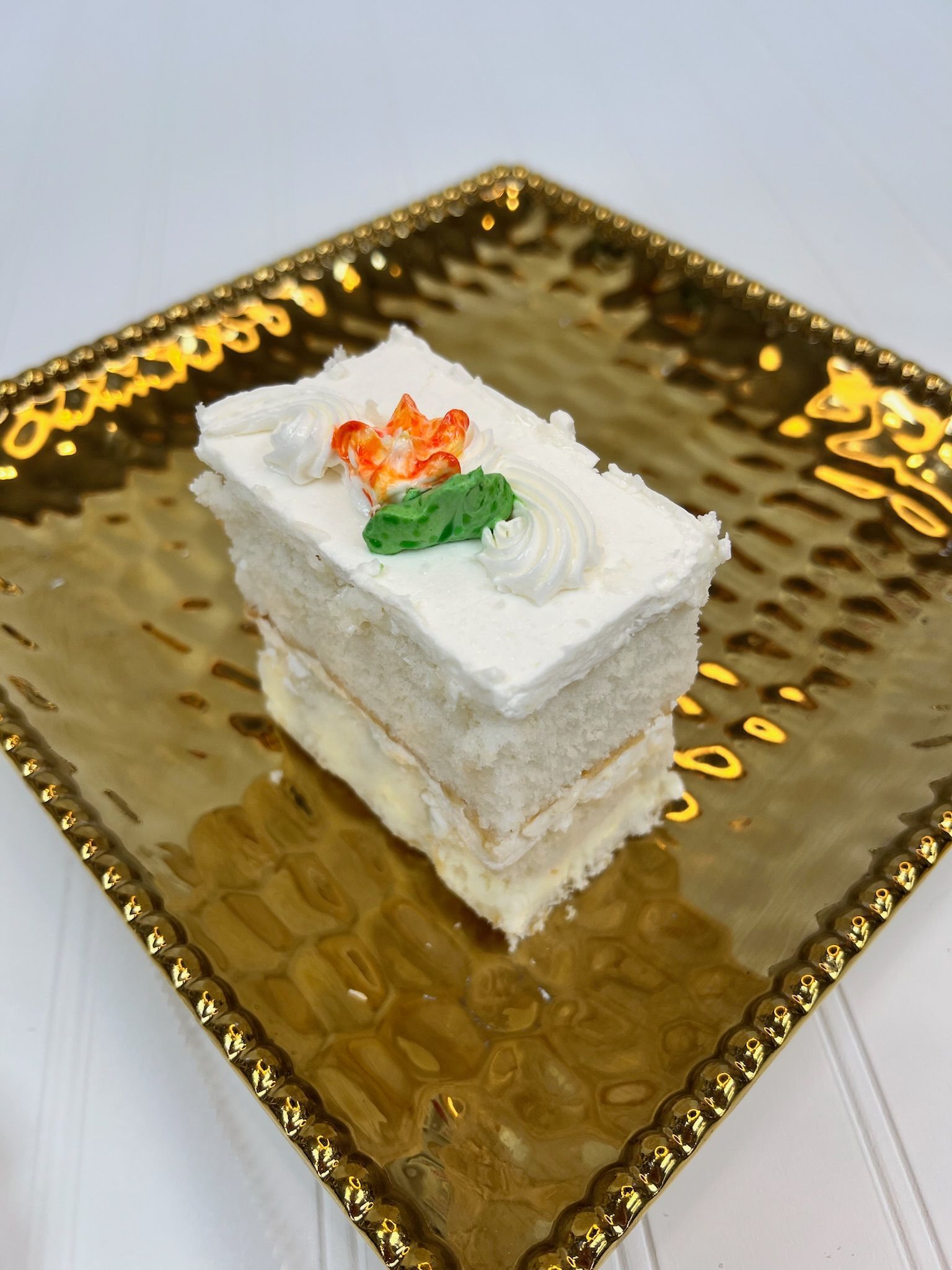 Cake slice with white frosting and orange and green decoration on a gold, textured plate.