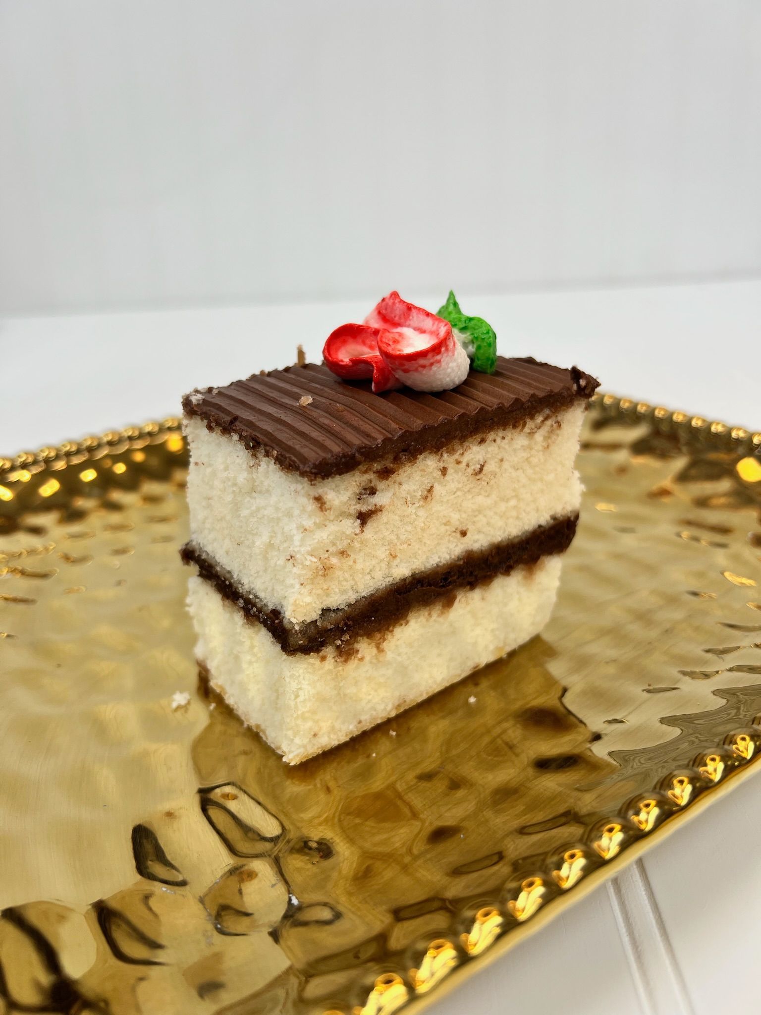 Cake slice with chocolate frosting and a strawberry decoration on a gold plate.