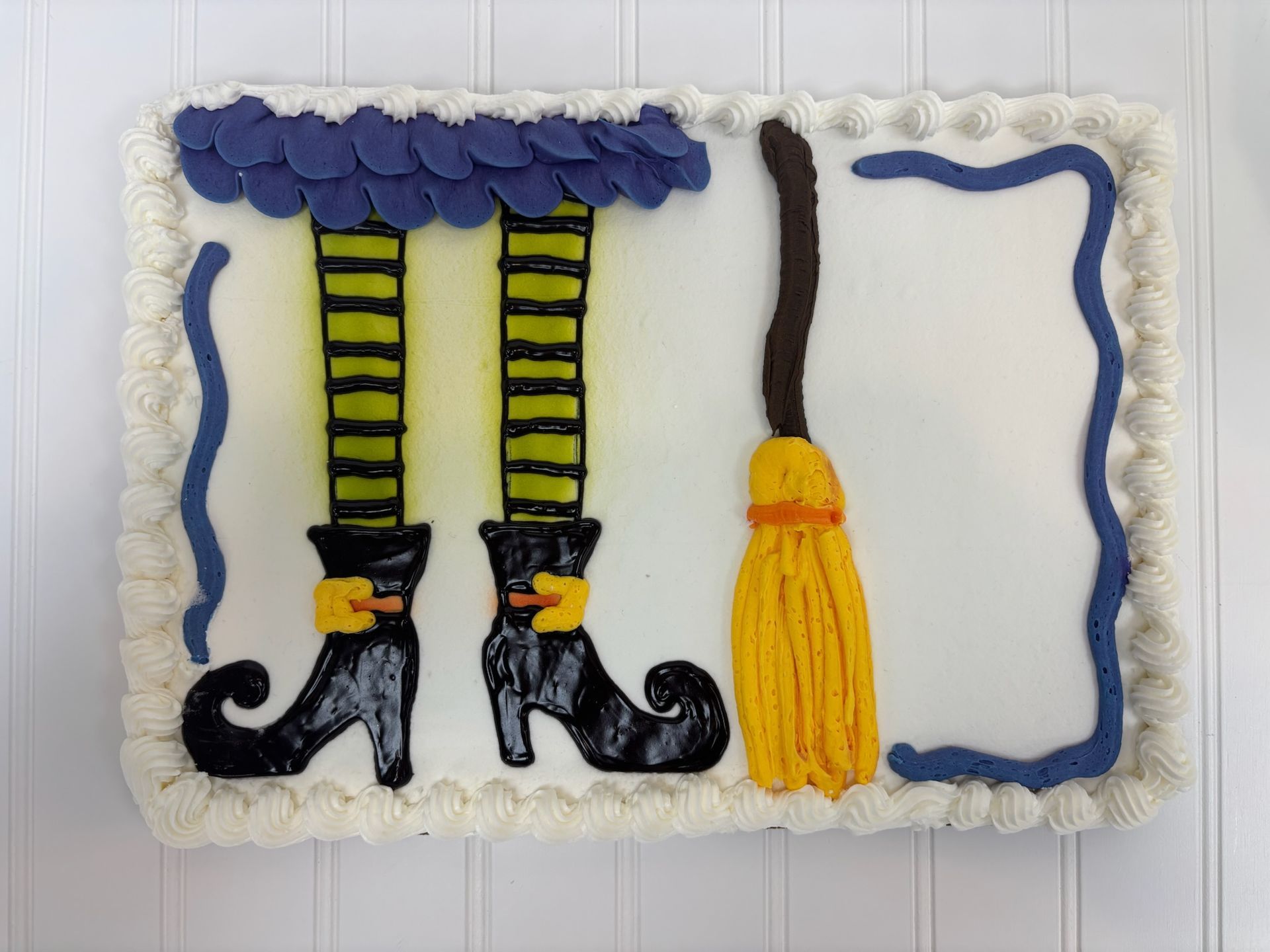 Cake decorated with witch legs, broom, and blue ruffled skirt.