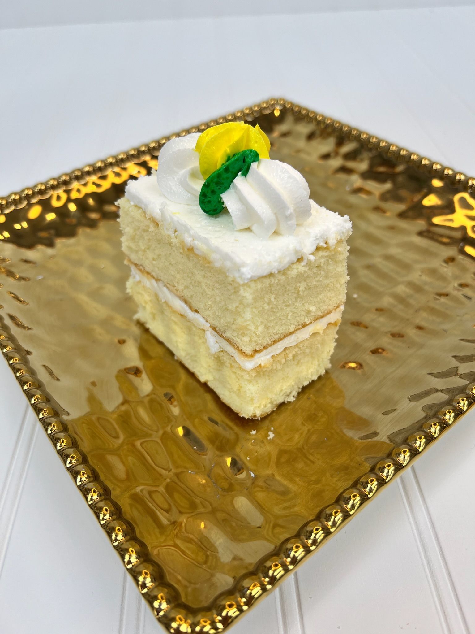 Slice of layered yellow cake with white frosting and a yellow and green decoration on a gold plate.