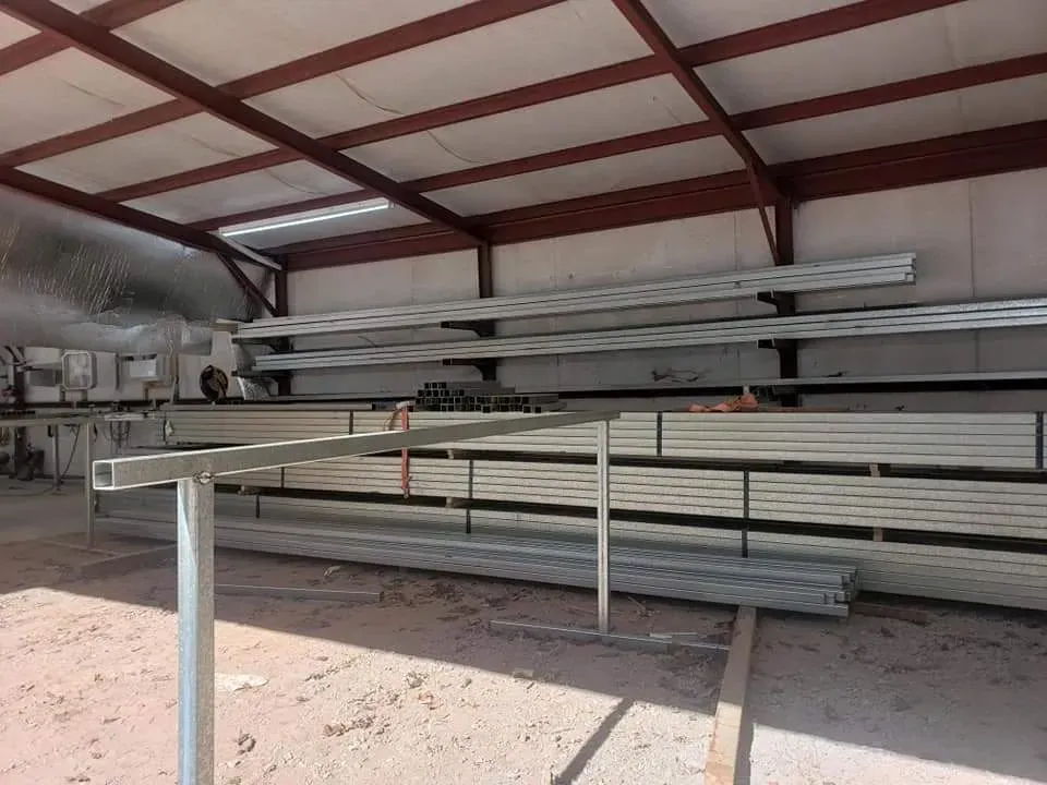 Stacked metal pipes under a red-roofed open shed with a white railing in front