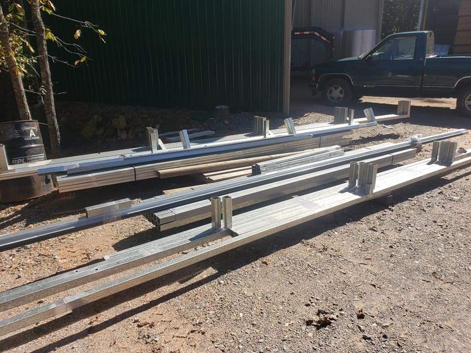 Metal beams stacked on dirt beside a green shed, with a pickup truck in the background.