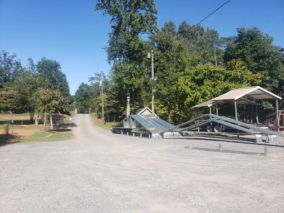 Gravel road with fallen utility poles beside a tree-lined rural street and open shelter