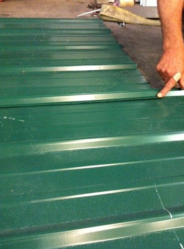Green corrugated metal roofing being installed, with a worker’s hand pointing along the seam