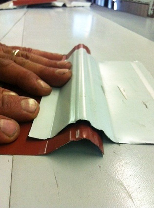 Hands shaping a white metal roof panel over a red trim piece on a worktable