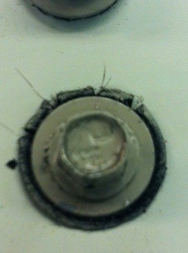 Close-up of a dirty round metal button or fixture on a pale surface