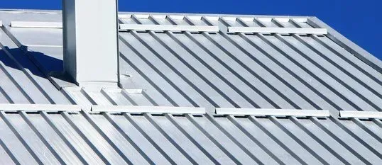 Silver corrugated metal roof with white roof rails and a chimney in bright sunlight