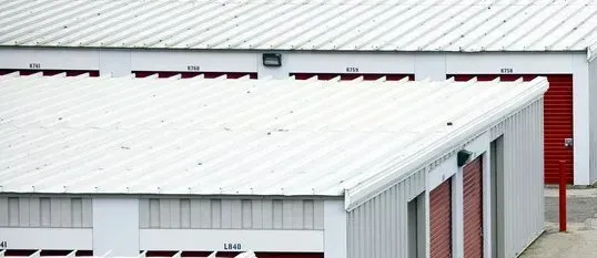 White metal-roofed industrial building with a row of red doors and beige siding