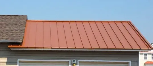 Copper-colored metal roof on a building, with a small section of shingled roof at the left edge.