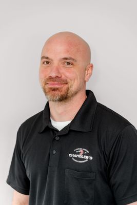A smiling person wearing a black polo shirt with a company logo, set against a plain light gray background.