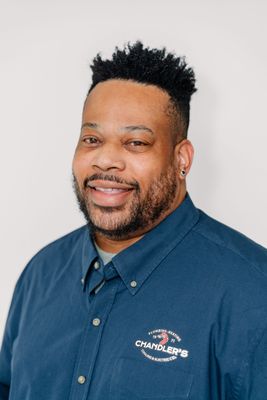 Smiling person wearing a blue short-sleeved button-down shirt with a small logo on the chest against a white background.