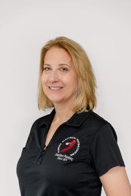 A smiling woman with shoulder-length blonde hair wearing a black polo shirt with a company logo.