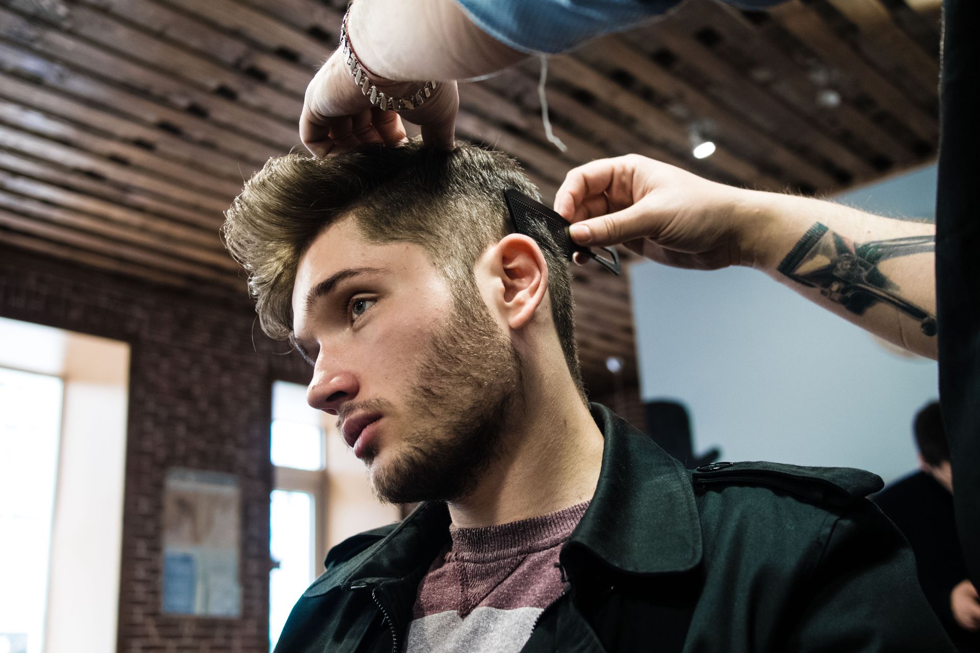 Stylist trimming a man’s hair in a barbershop, with exposed brick and a wood ceiling in the background.