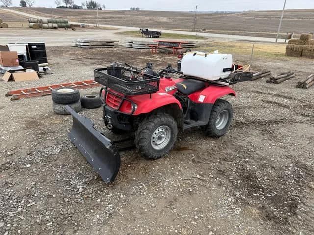 A red atv with a plow attached to it is parked in a dirt field.