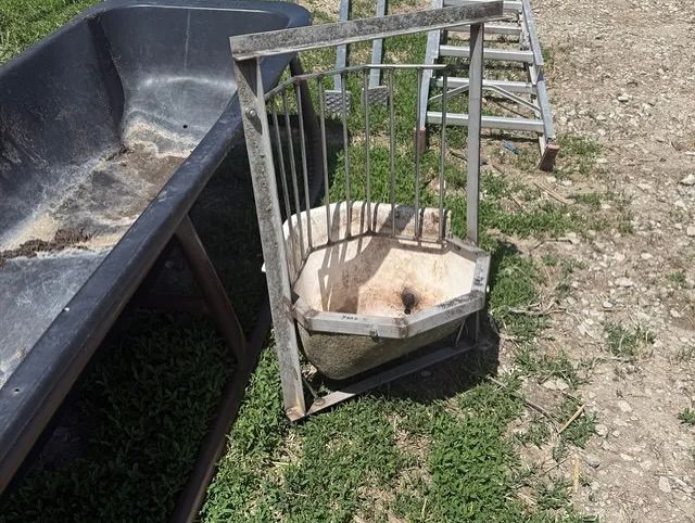 A sheep feeder is sitting in the grass next to a ladder.
