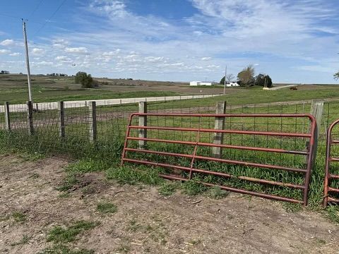 A red gate is sitting in the middle of a grassy field next to a fence.