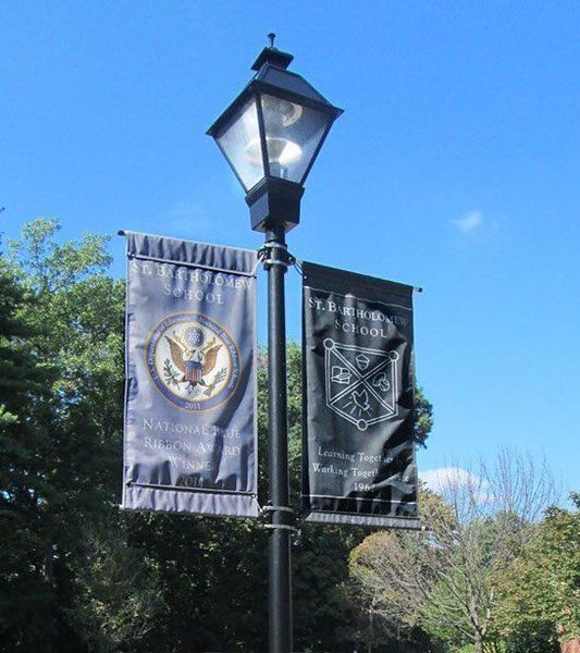 Lamppost with banners: one with US seal, other with school crest, against a blue sky.