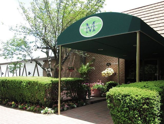 Entrance to a building with a green awning, brick facade, and manicured hedges.
