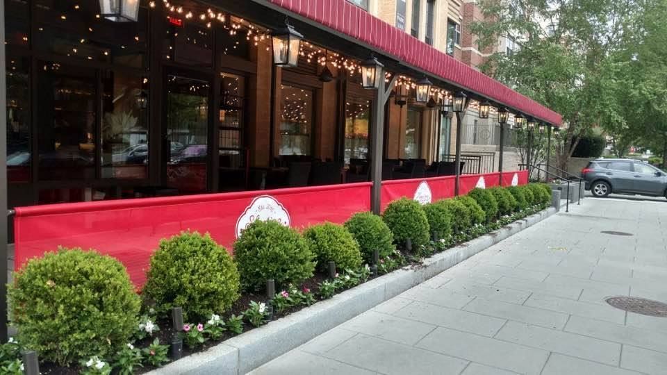 Exterior of a restaurant with red awning, hedges, and sidewalk.